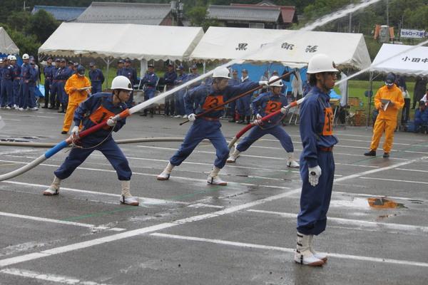 篠山市消防団の3名が、横に並び、真ん中の人が棒のような物をもち両隣の2人が放水している前に指揮官がいる写真